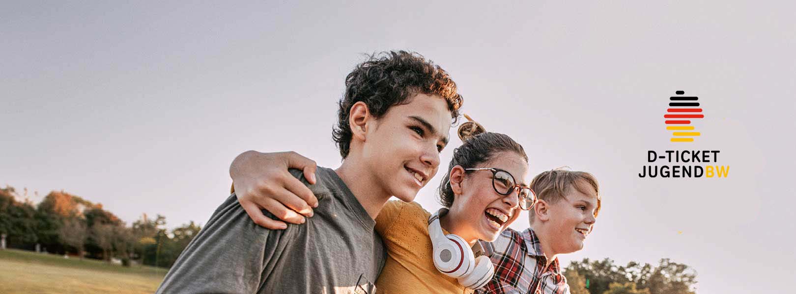 3 lachende Schülerinnen und Schüler auf einer Wiese