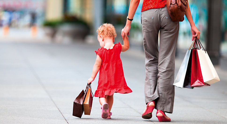 kleines Mädchen im roten Kleid an der Hand einer Frau  mit Einkaufstüten